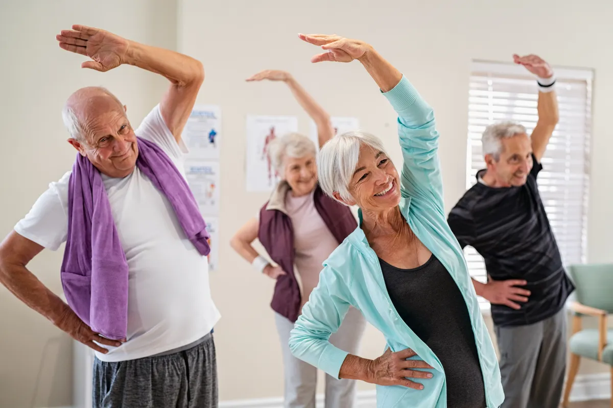 A group of smiling older adults stretching during an indoor exercise class