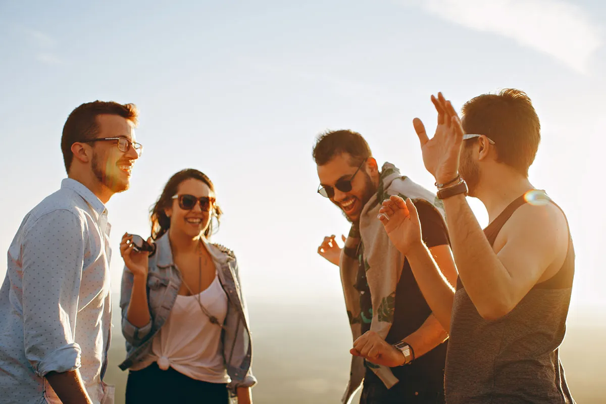 A group of friends laughing together outdoors in sunlight