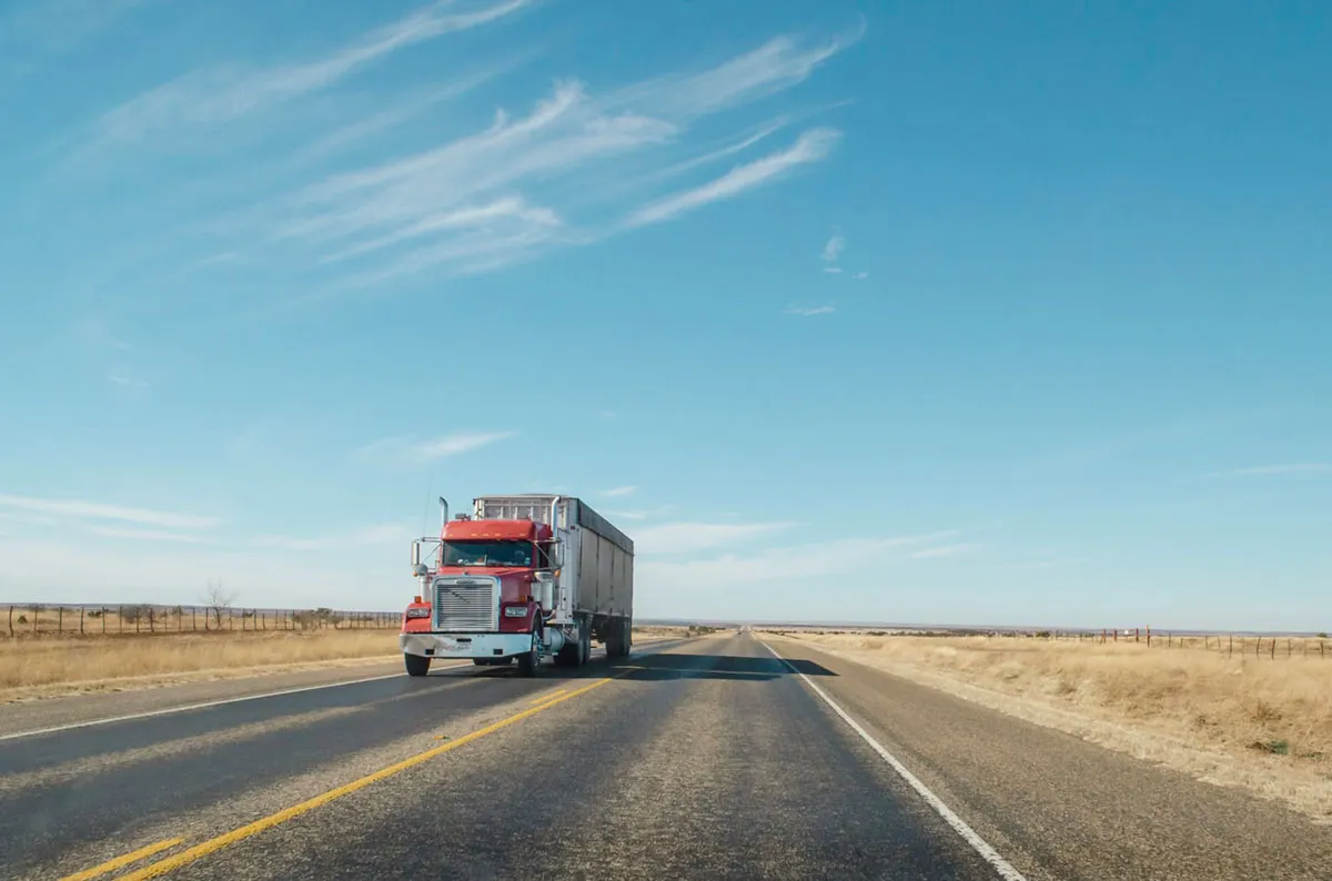 A semi truck driving on a straight highway under a wide sky