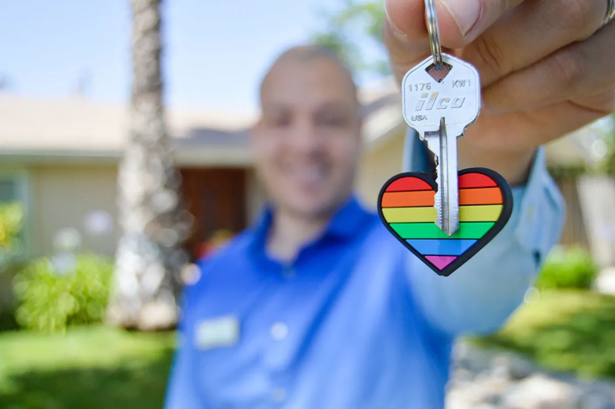 A man holding out a house key on a rainbow heart keychain