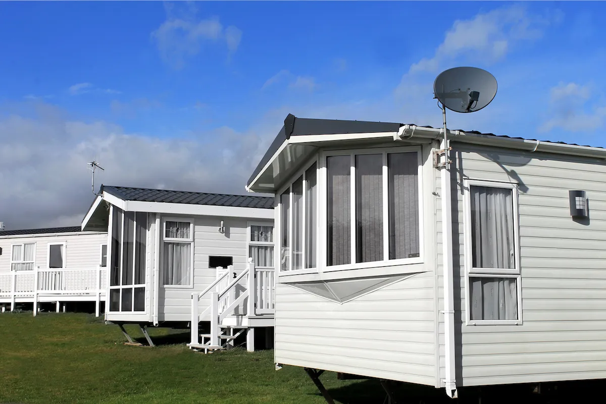 Two white mobile homes on a lot under a blue sky