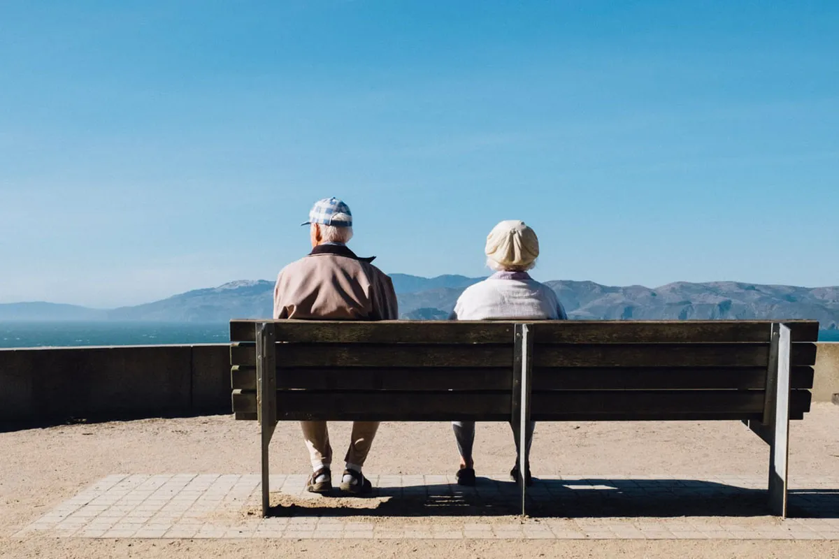 An older couple sitting on a bench overlooking the coast