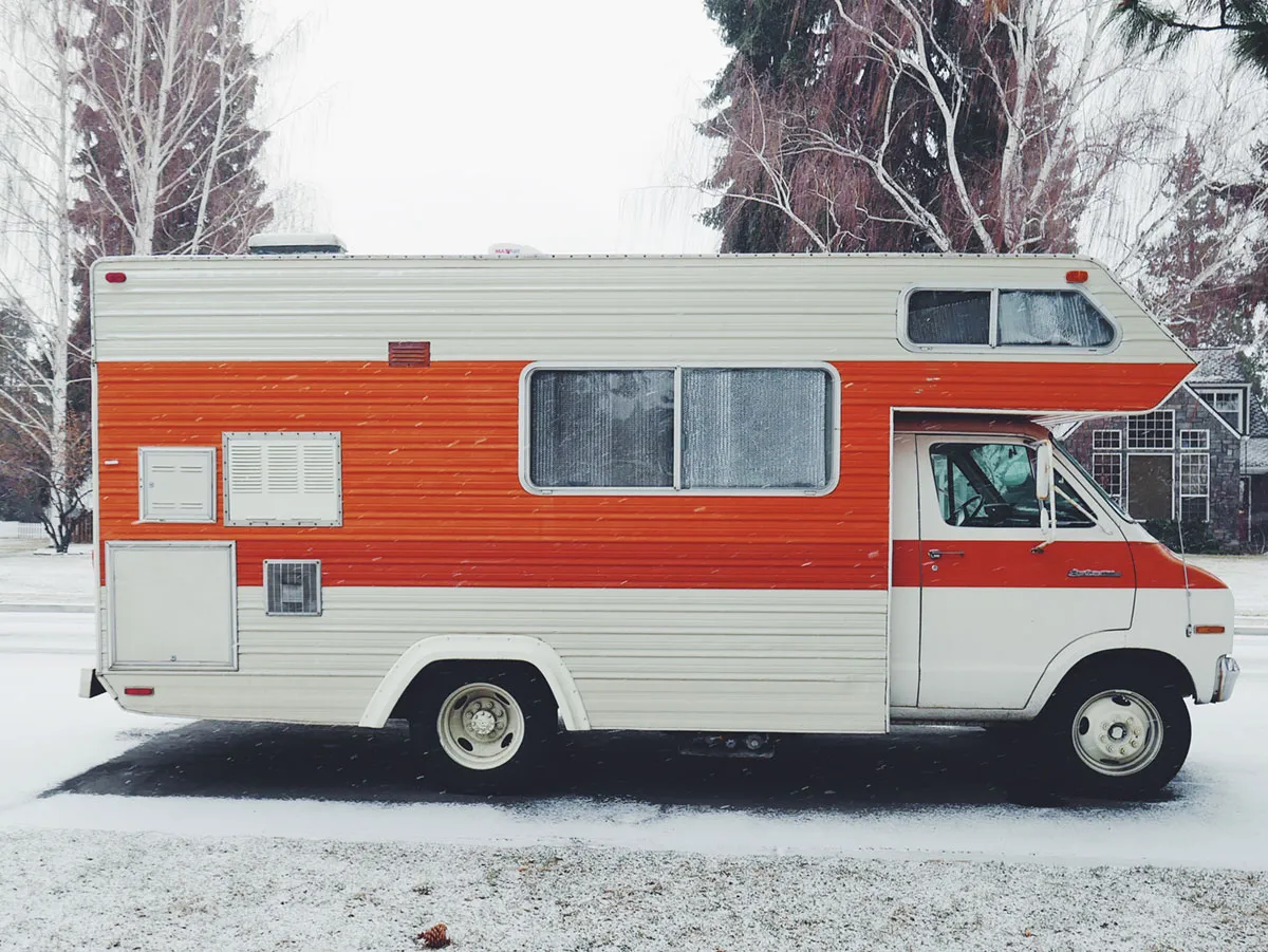 An orange and white RV parked in a snowy driveway