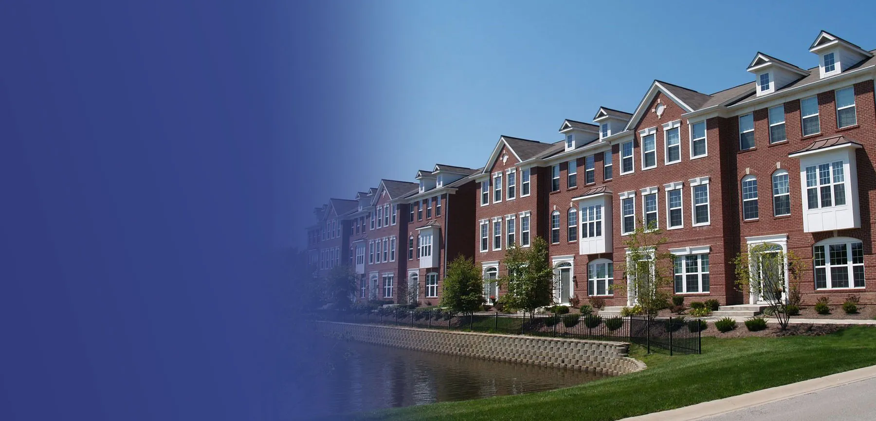 A row of brick townhomes along a landscaped waterfront walkway